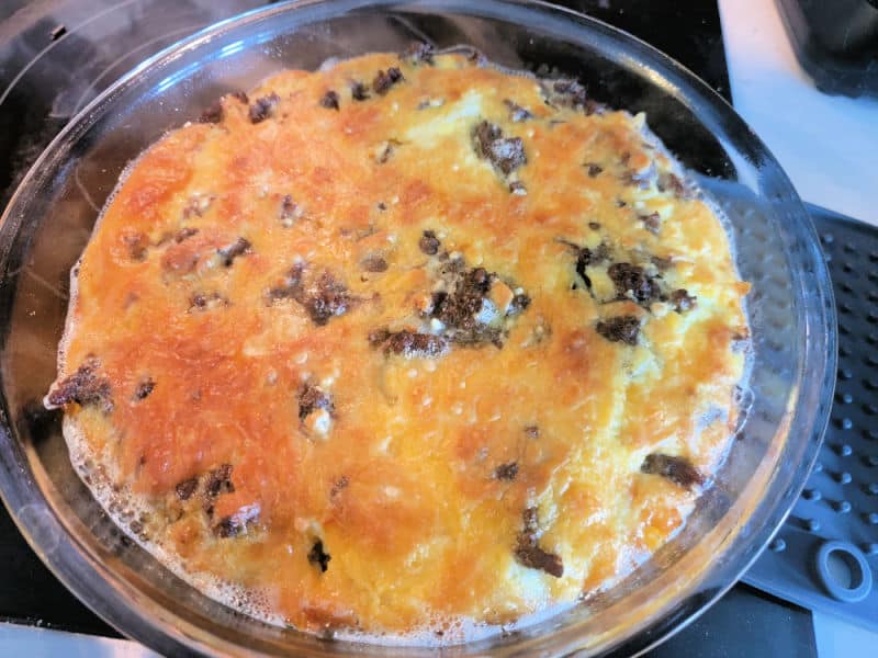 Impossible cheeseburger pie in a glass pie dish on the stovetop after baking