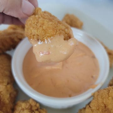 Chicken nugget dipping into Boom Boom sauce in a white bowl
