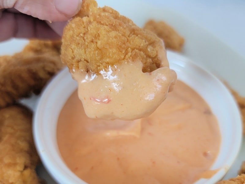 Chicken nugget dipping into Boom Boom sauce in a white bowl 