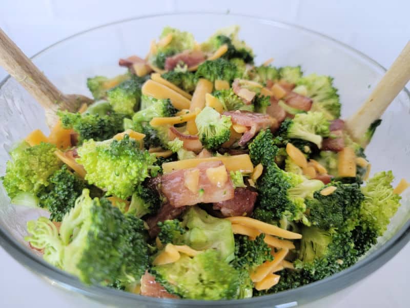 Broccoli bacon salad with cheddar cheese in a glass bowl with wooden spoons