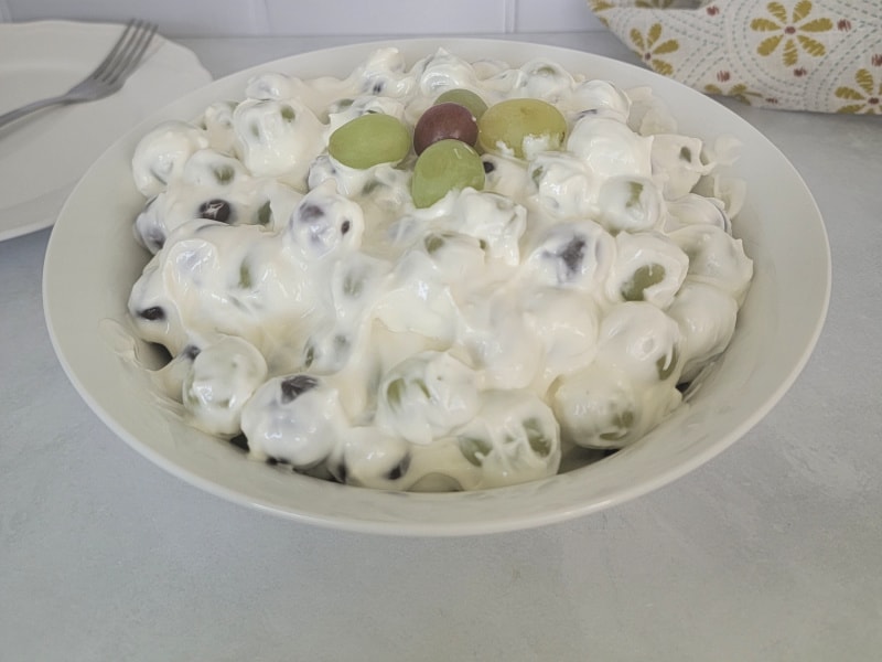 Grape salad in a white bowl next to a plate and fork and a cloth napkin