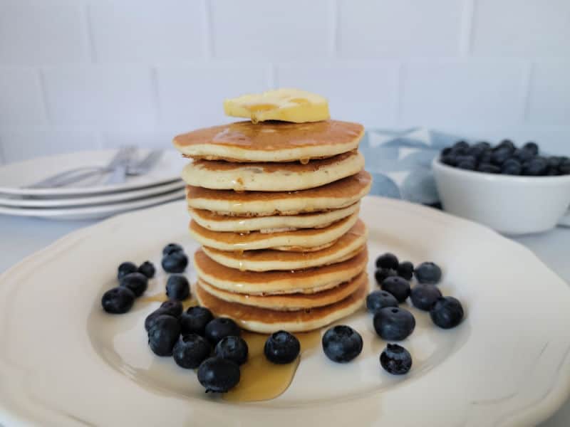 Stack of pancakes on a white plate with syrup and blueberries