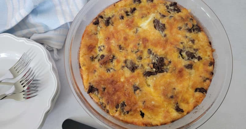 Impossible cheeseburger pie in a glass pie pan next to a stack of white plates and forks