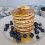 stack of air fried pancakes on a white plate with syrup, butter, and blueberries