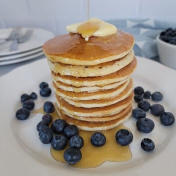 stack of air fried pancakes on a white plate with syrup, butter, and blueberries