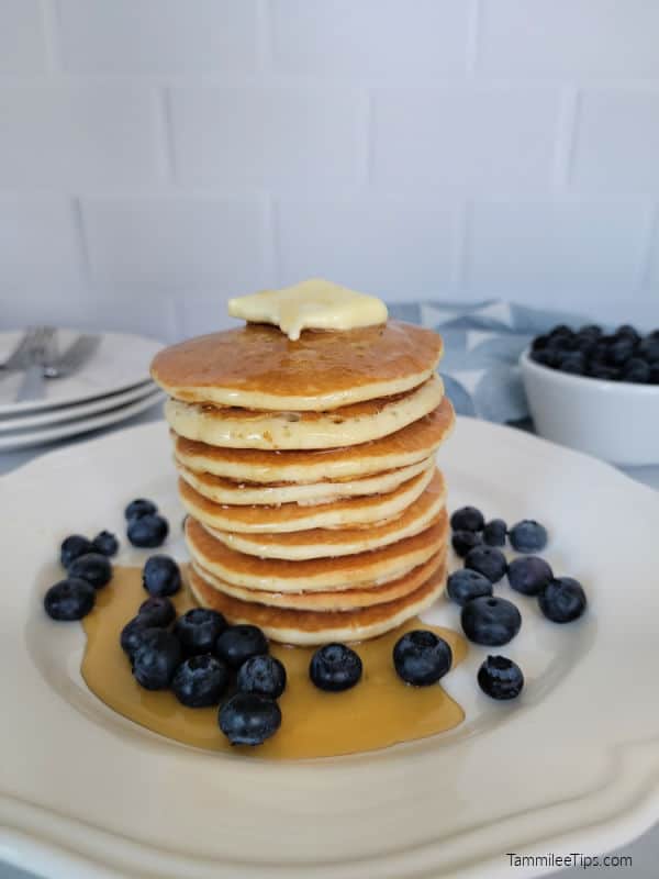 Stack of pancakes on a white plate with syrup and blueberries