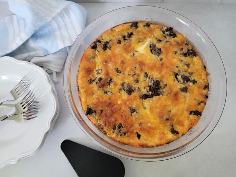 Impossible cheeseburger pie in a glass pie dish next to a stack of white plates and forks