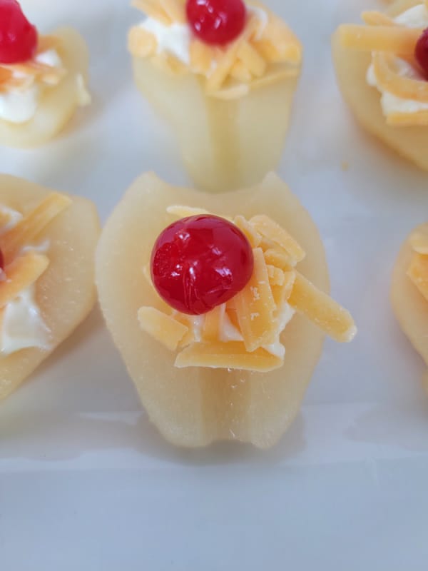 maraschino cherry on cheddar cheese on a pear half on a white platter. 
