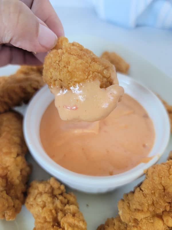 Chicken nugget dipping into Boom Boom sauce in a white bowl 