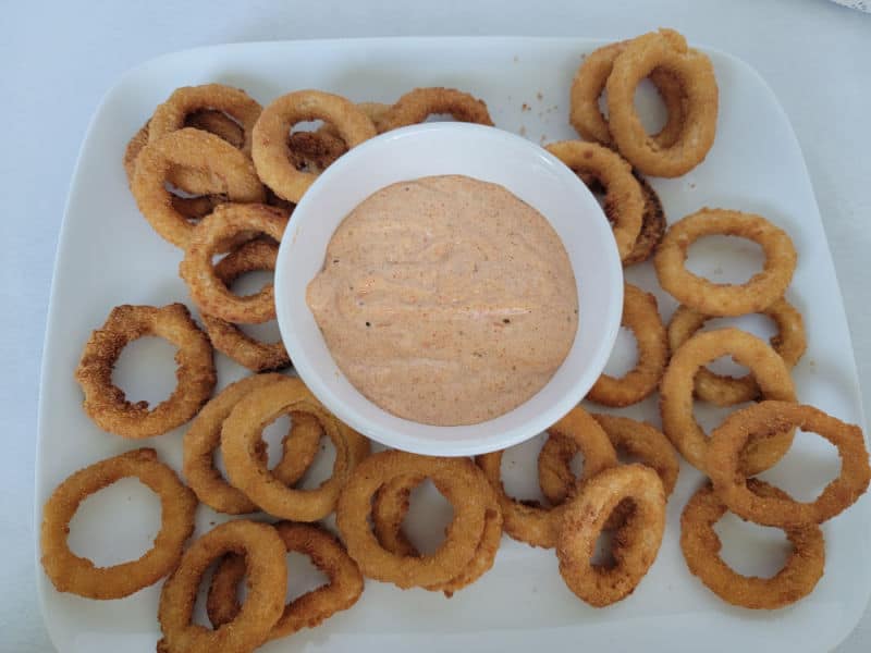 a plate with onion rings and dipping sauce in a bowl 