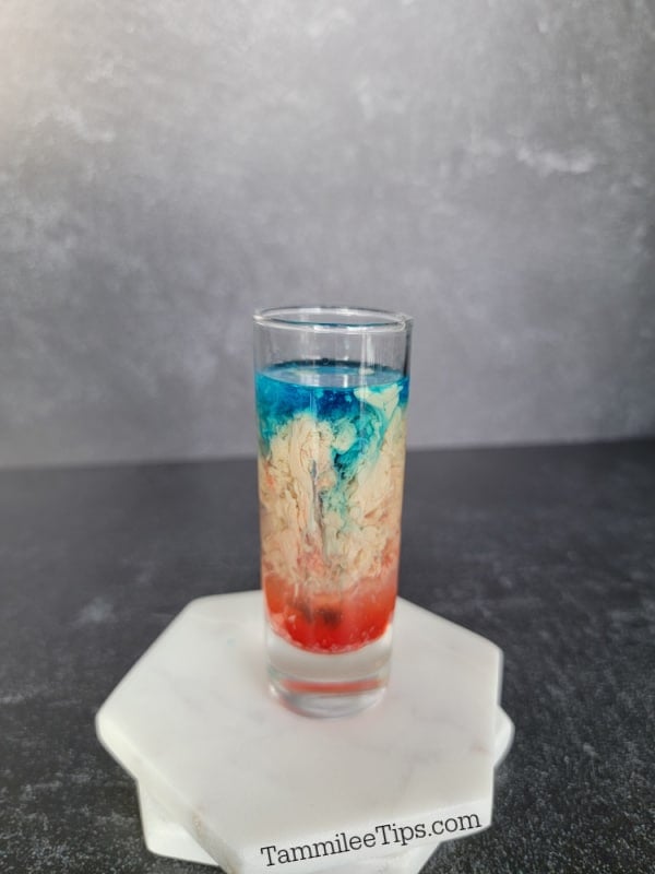blue liquid floating on cream and red liquid in a shot glass on two coasters