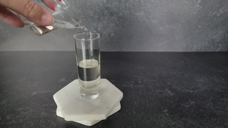 Clear liquid pouring into a shot glass on a marble coaster 