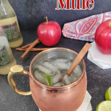 Apple cider mule text over a bottle of ginger beer, apples, cinnamon sticks, and an apple cider mule in a copper mug with ice