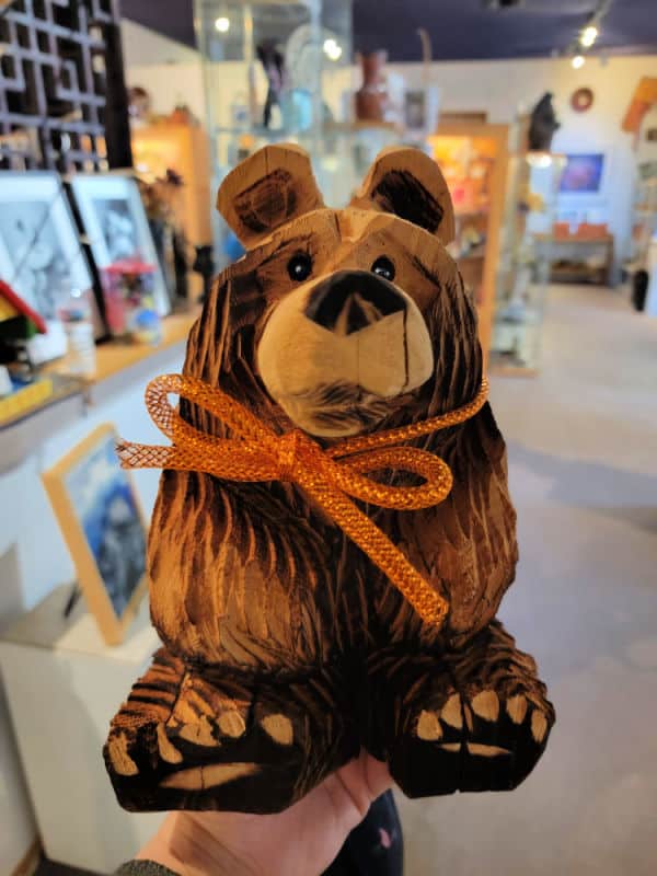 Wooden carved bear with an orange ribbon around its next in an art gallery
