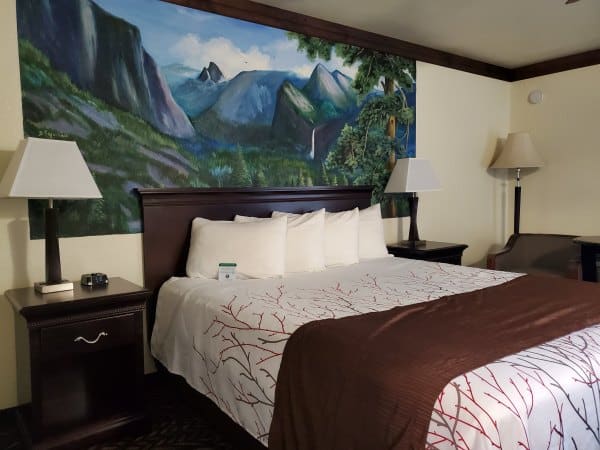 Yosemite mural painted above a bed with pillows and a nightstand with a lamp