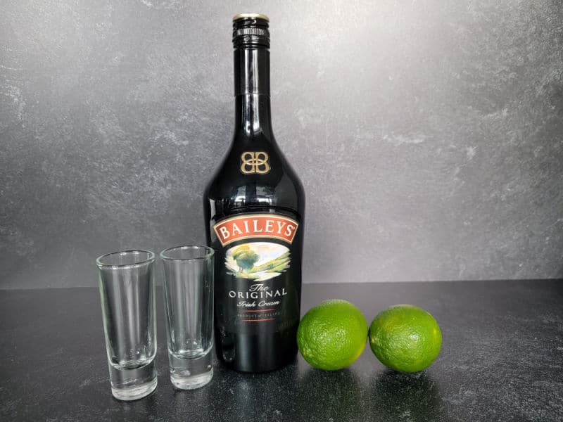 Cement Mixer Shot ingredients with two glass shot glasses, Baileys Irish Cream and two limes