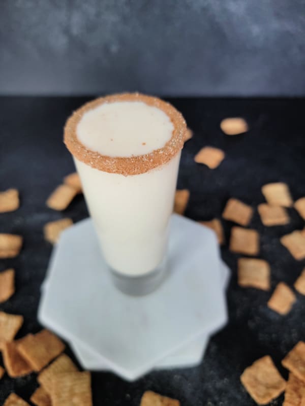 cinnamon toast crunch shot in a shot glass on marble coasters with cereal spread around it