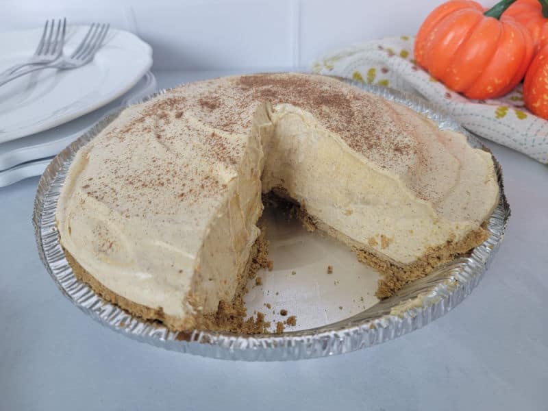 No bake pumpkin pie in a pie dish with a slice missing next to a stack of plates and forks