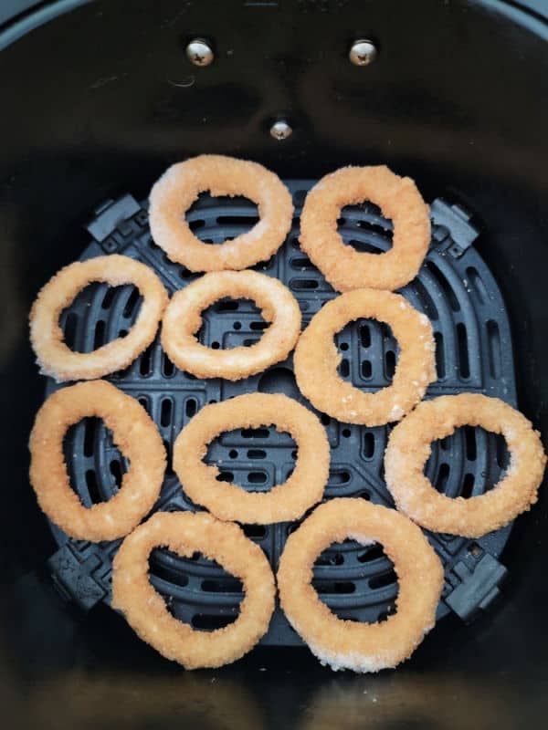 frozen onion rings spread in an air fryer basket