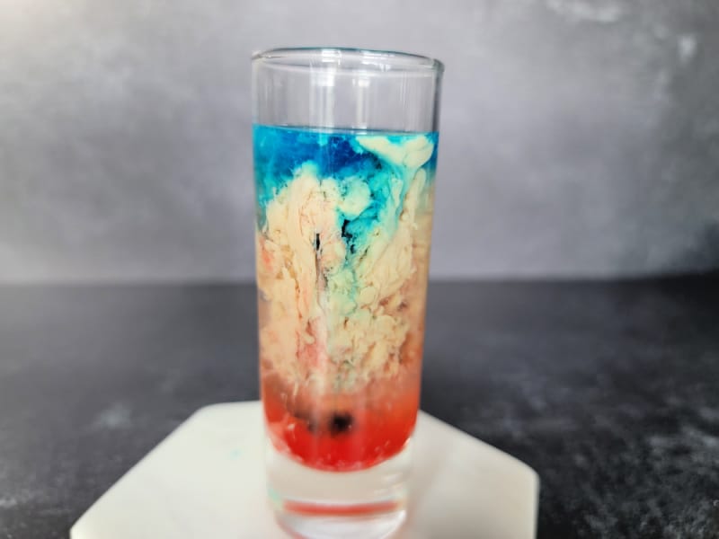 blue, cream, and red liquid swirling in a glass shot glass sitting on a marble coaster