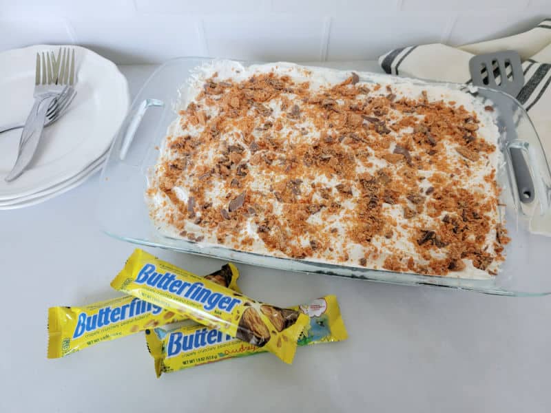 Butterfinger Poke Cake in a glass 9x13 cake pan next to a stack of butterfinger candy bars