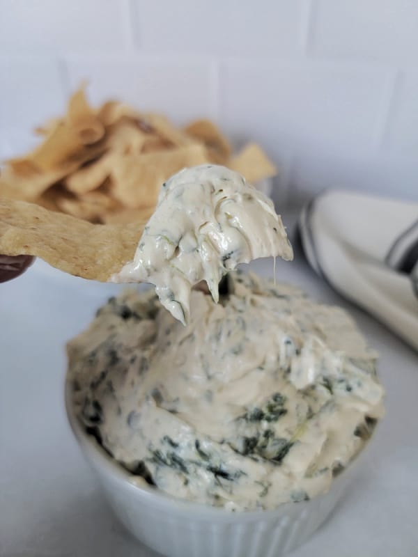 Tortilla chip holding Knorr Spinach Dip over a bowl of dip