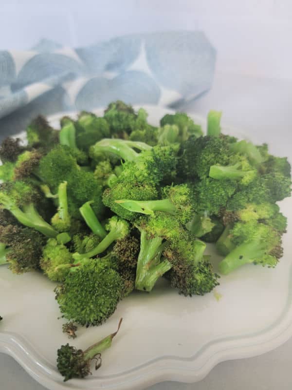 Air fried broccoli on a white plate next to a cloth napkin