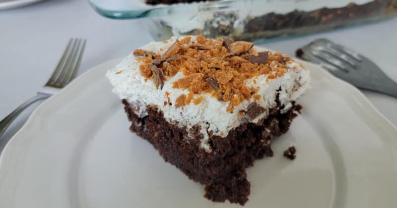 square of Butterfinger poke cake on a white plate next to forks