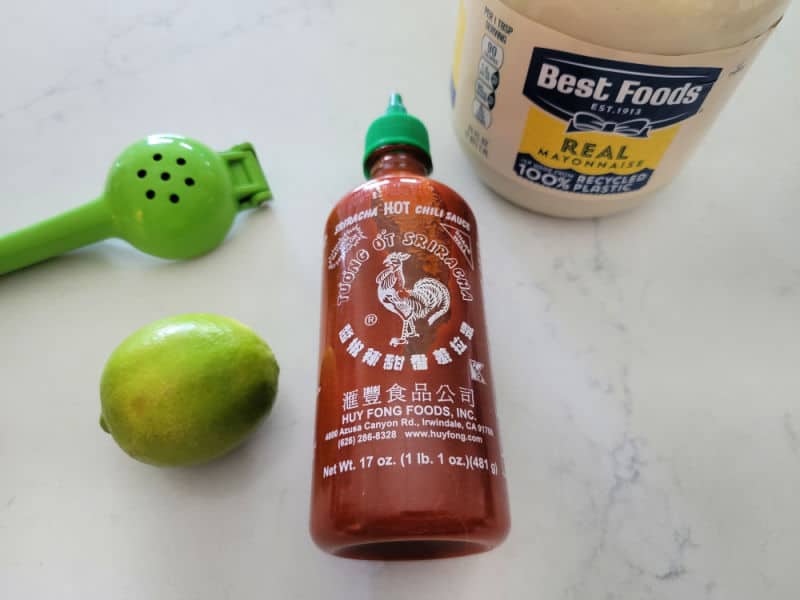Lime juicer, lime, sriracha, best foods real mayo container on a white counter. 