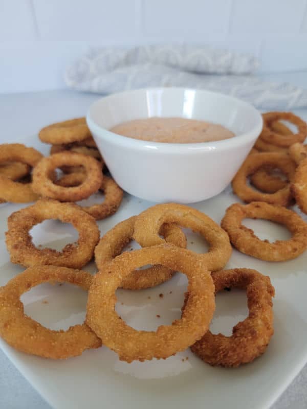 a plate with onion rings and dipping sauce in a bowl 