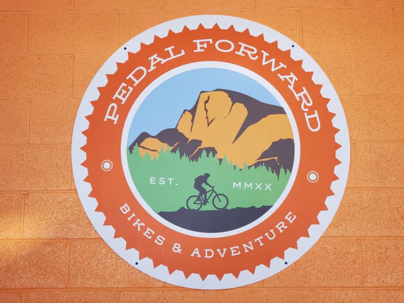 Pedal Forward Bike & Adventure sign with a mountain and figure on a bike
