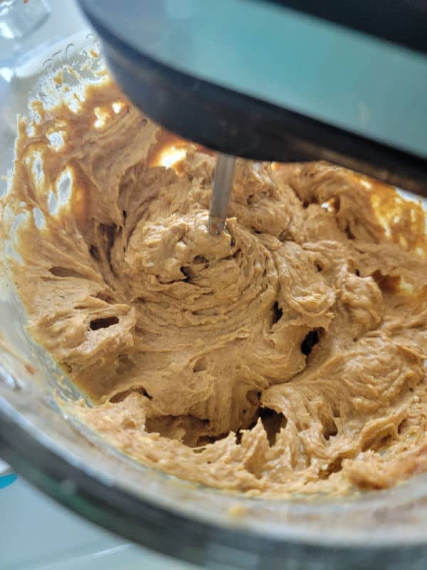 Hand mixer mixing pumpkin dip in a glass bowl