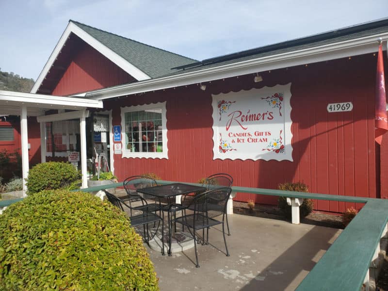 Reimers Candies, gifts, and ice cream sign on a red building with a black table and chairs in front