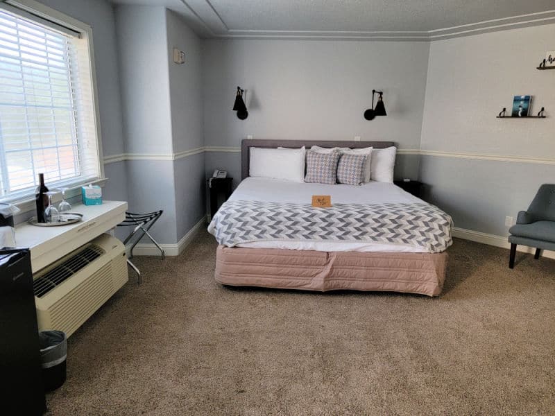 bed in the middle of a room with a counter holding wine and glasses near a chair