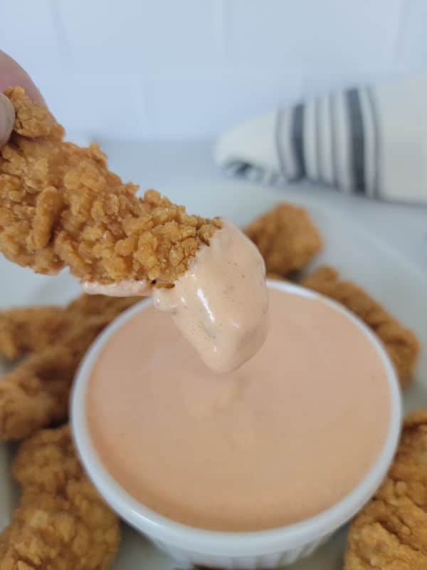 Chicken tender dipping into a white bowl filled with a mayo substance. 