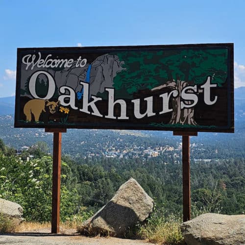 Welcome to Oakhurst sign with a bear, waterfall and tree
