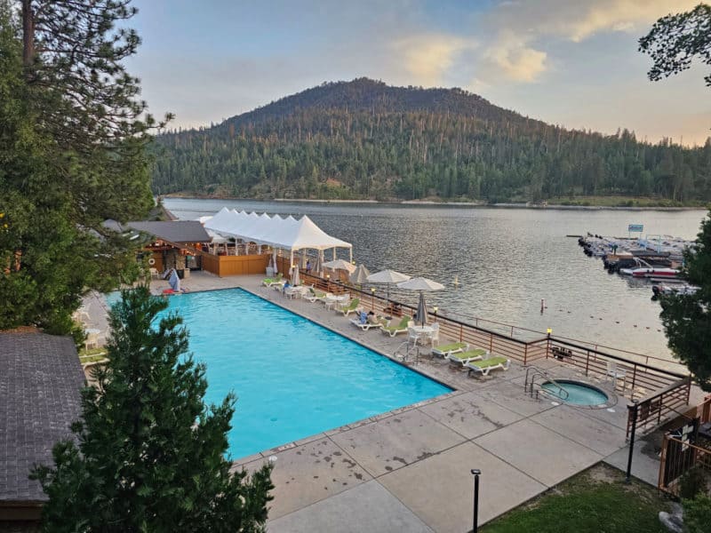 Swimming pool and deck next to a lake with a mountain in the background