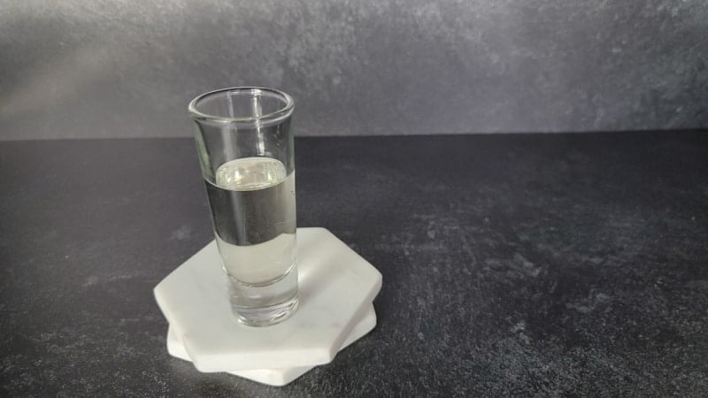 Clear liquid in a shot glass on two marble coasters