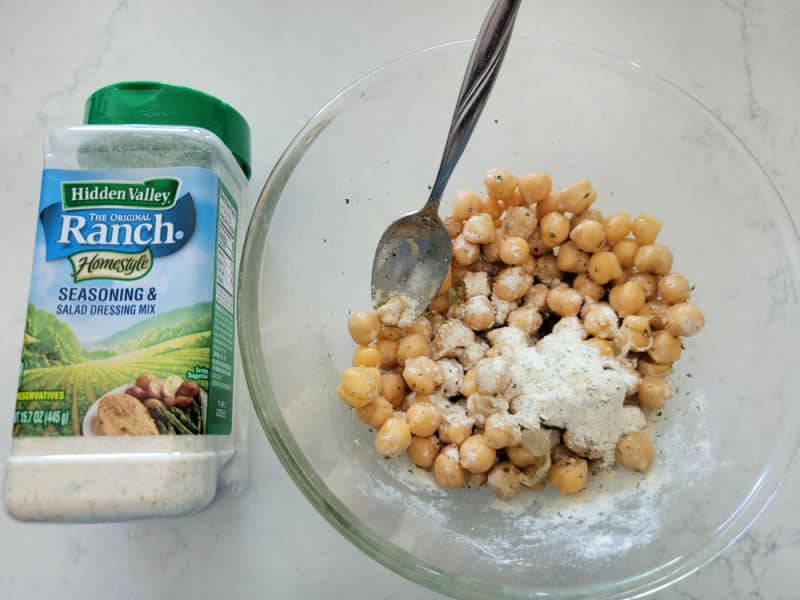 Hidden valley ranch dressing next to a glass bowl with chick peas, seasoning, and a spoon