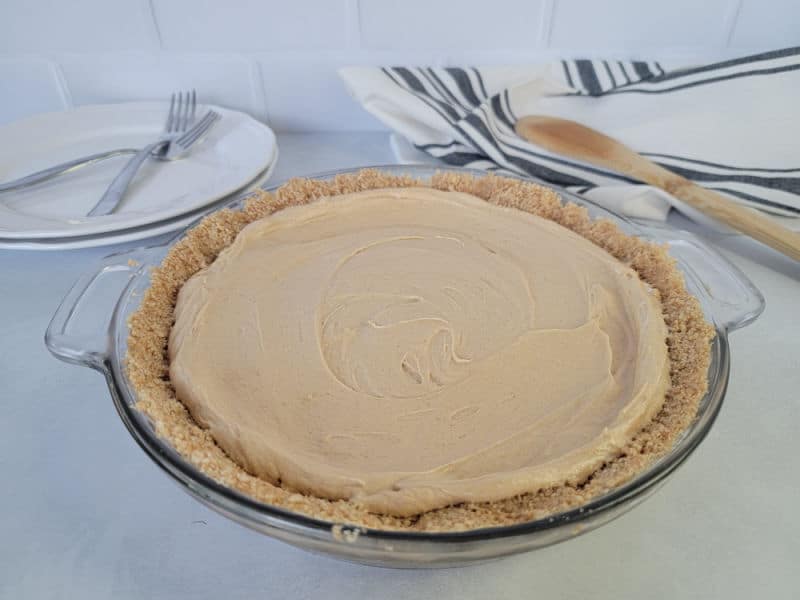 peanut butter pie in a graham cracker crust in a glass baking dish on a white counter with plates and forks in the background. 