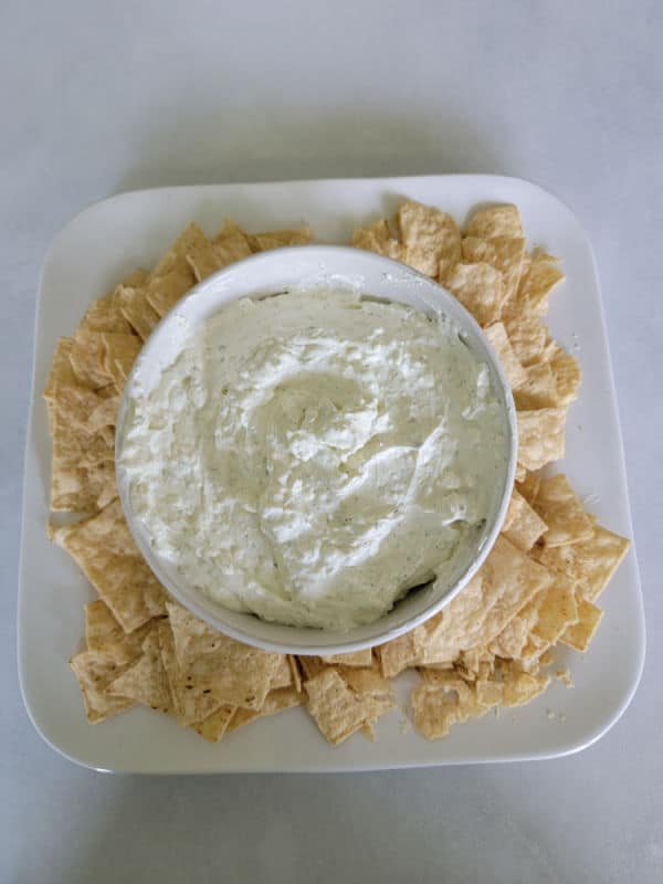 Ranch dip in a white bowl with tortilla chips on a white plate