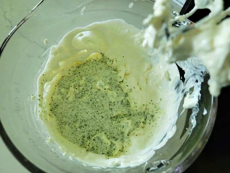 Dry ranch seasoning mix over cream cheese and sour cream mixture in a glass bowl