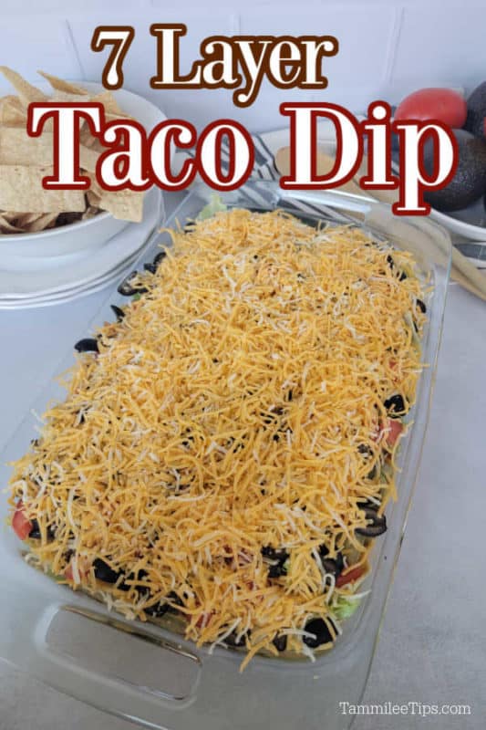 7 layer taco dip text over a glass baking dish with shredded lettuce on top of dip, next to a bowl of tortilla chips