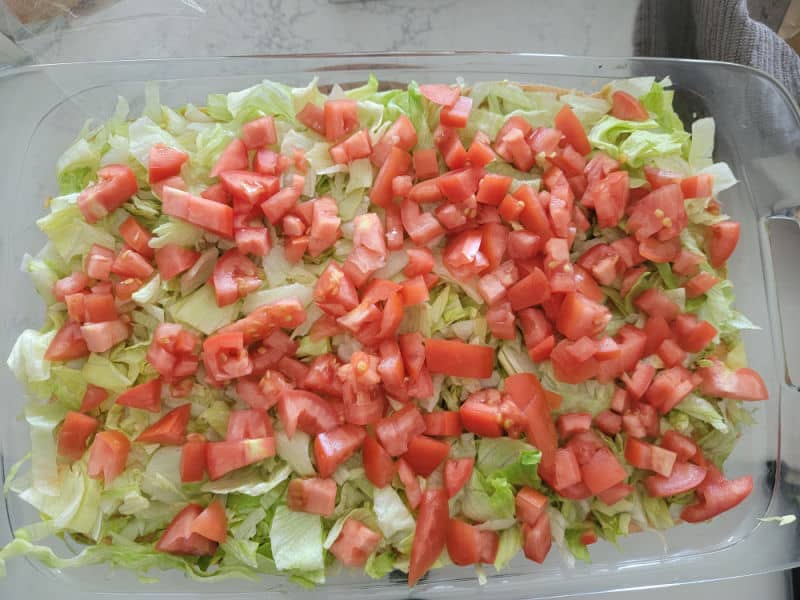Diced tomatoes spread over shredded lettuce in a glass baking dish