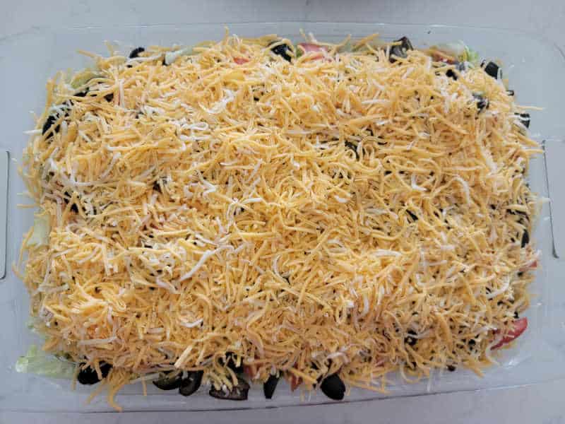 Shredded cheese over olives and lettuce in a baking dish