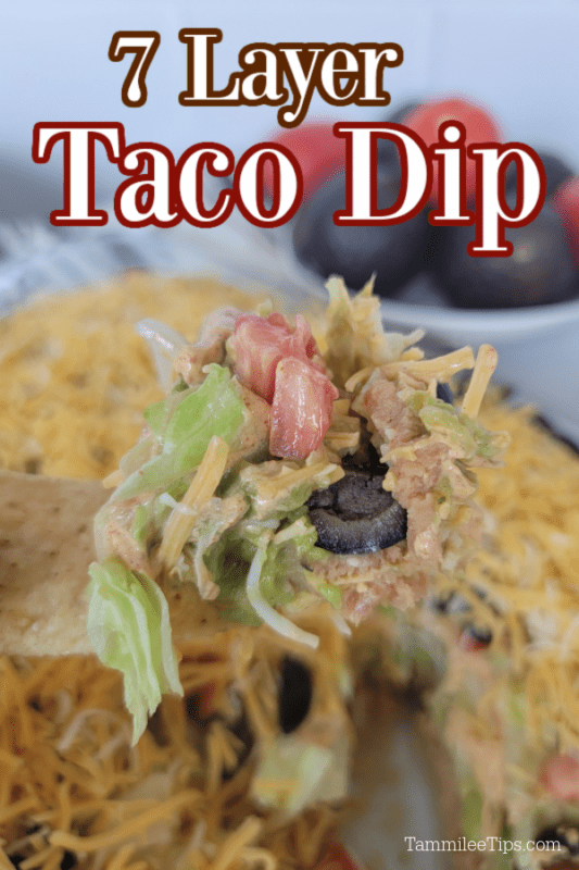 7 Layer Taco Dip over a tortilla chip holding dip with tomatoes, lettuce, meat, and olives