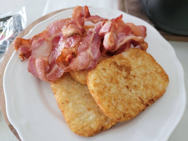 Air fryer basket on a white plate with hashbrowns. 