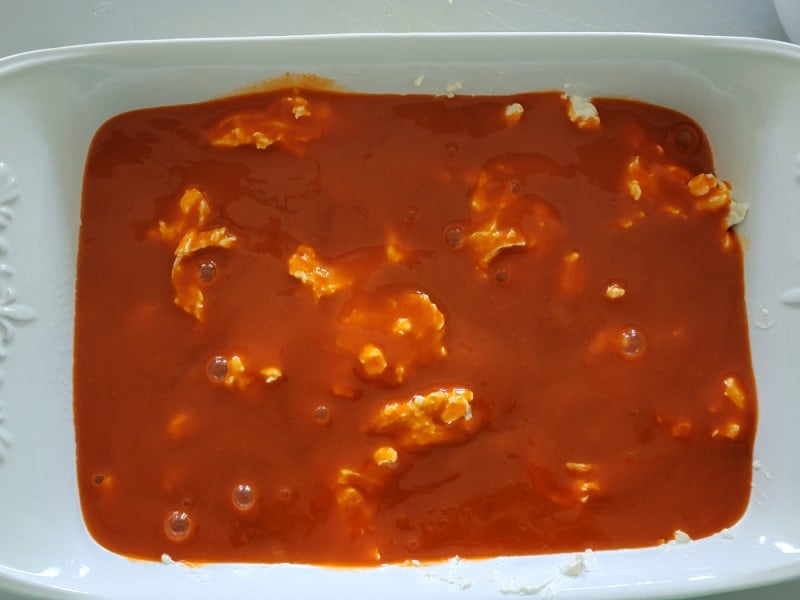 Franks Red Hot Buffalo Sauce spread over shredded chicken in a casserole dish for Buffalo Chicken Dip