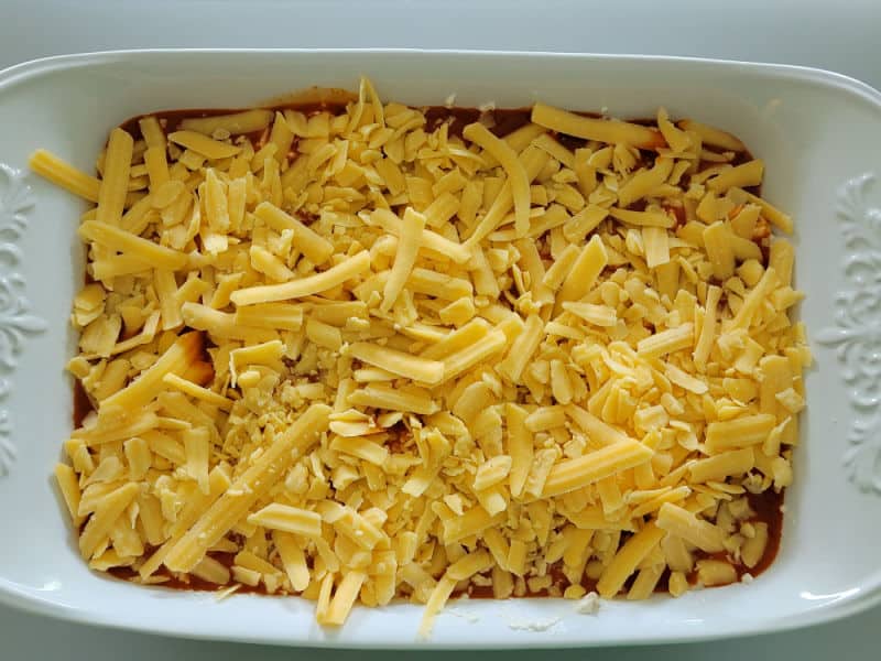Shredded cheddar cheese spread over Franks Buffalo Sauce in a white casserole dish for Buffalo Chicken Dip 