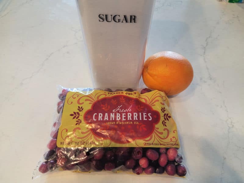 Cranberry relish ingredients, sugar, orange, cranberries on a white counter